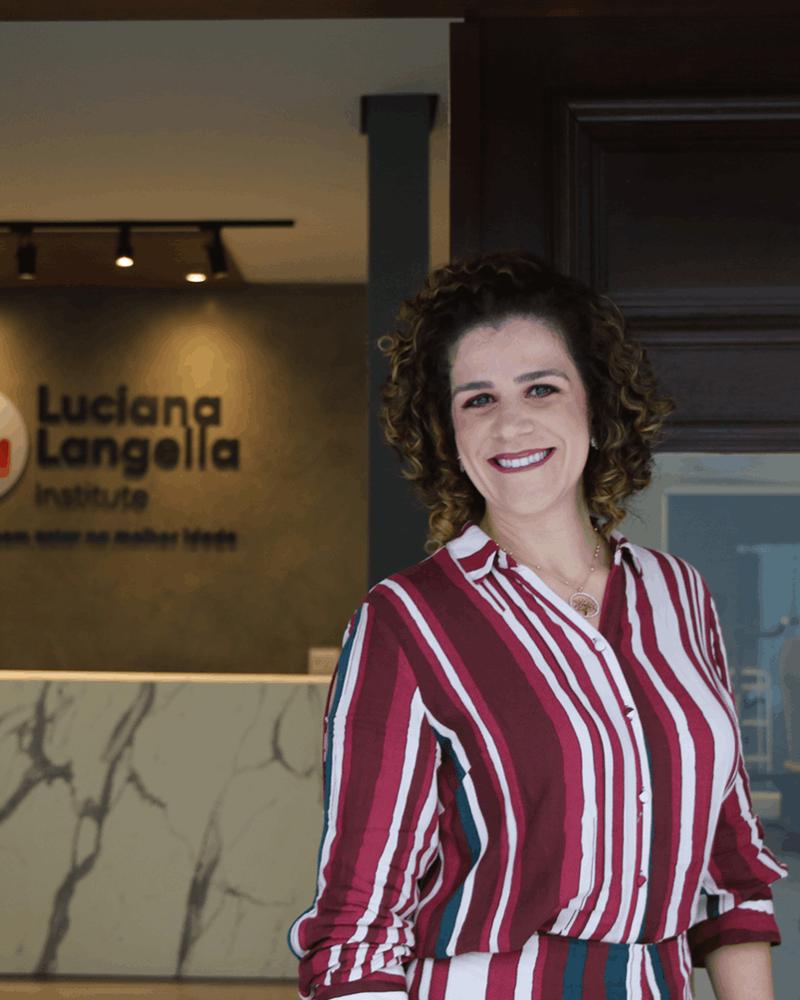 Luciana Langella na recepção da clínica, com o logo do instituto ao fundo
