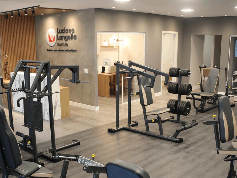 Salão de musculação da clínica, com os aparelhos em primeiro plano e a recepção ao fundo